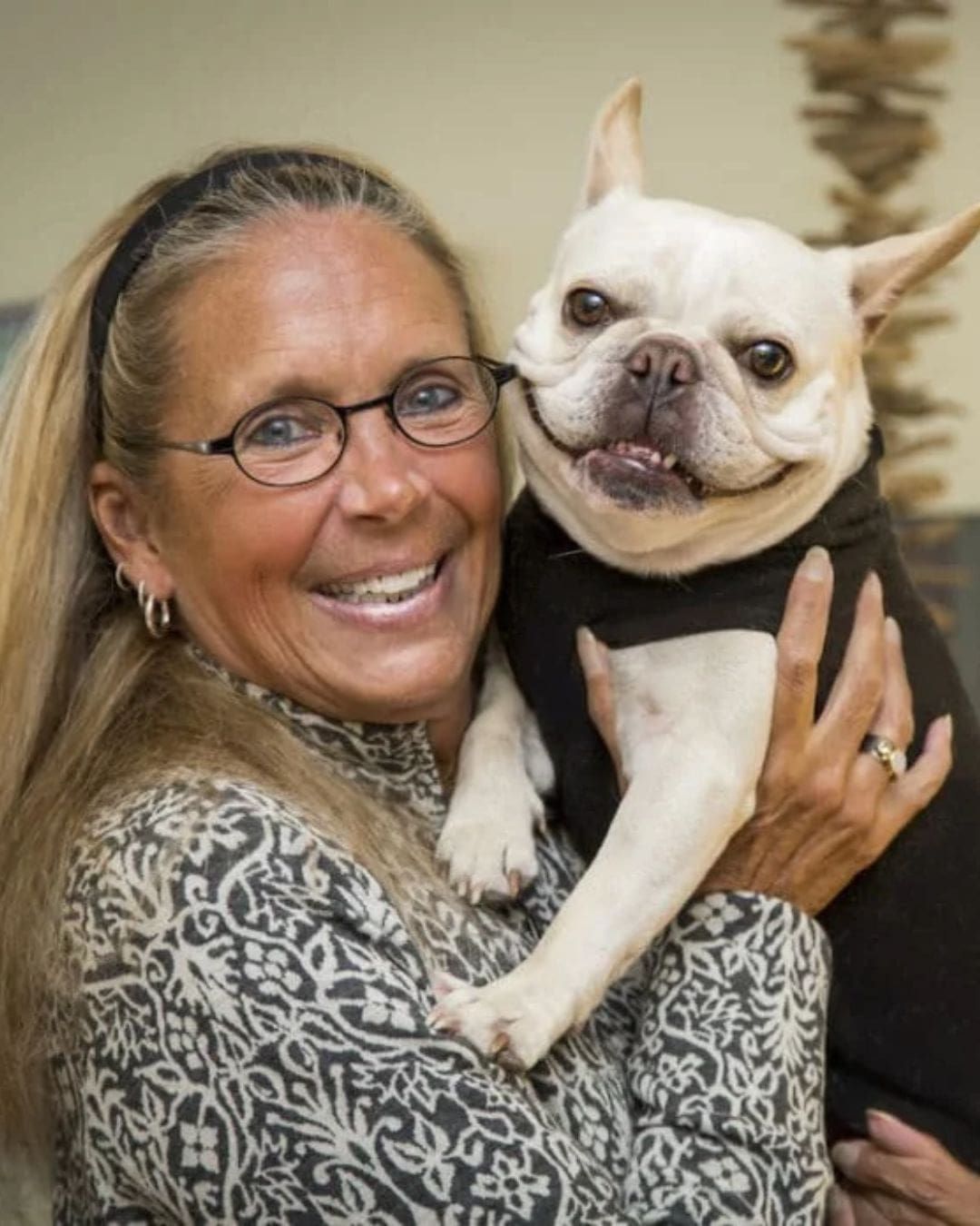 Dr. Susan Marra, a functional medicine doctor in Seattle, smiles while holding a white French Bulldog wearing a black sweater, indoors.