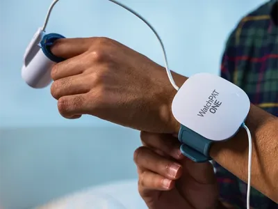 Affiliates 9 A person attaches a WatchPAT ONE sleep apnea monitoring device to their wrist and finger, preparing for a sleep study at home.