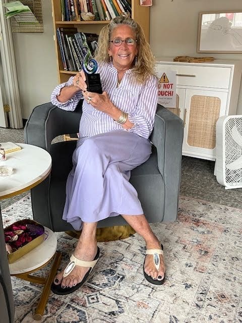 Dr. Susan Marra sitting in her office holder a blue, green, and black award 